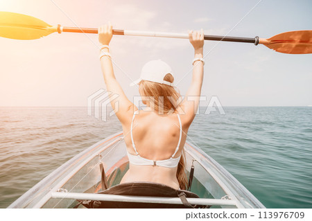 Woman in kayak back view. Happy young woman with long hair floating in transparent kayak on the crystal clear sea. Summer holiday vacation and cheerful female people relaxing having fun on the boat Woman in kayak back view. Happy young woman with long hair floating in transparent kayak on the crystal clear sea. Summer holiday vacation and cheerful female people relaxing having fun on the boat 113976709