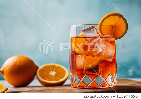 Orange Aperol cocktail with ice cubes and orange slices in a glass. Indoors in a photo studio on a table, copy space 113977650