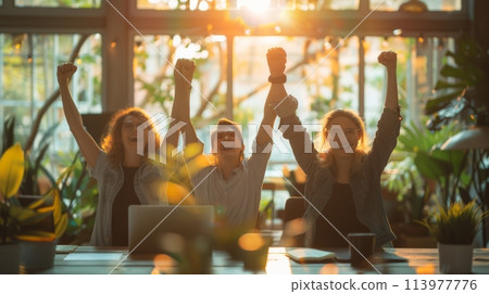 Business team celebrating a victory with raised arms in a modern workplace at sunset 113977776