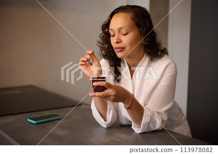 Portrait of a multi ethnic pretty woman in the morning at home, eating delicious tasty wholesome chocolate vegan yoghourt for breakfast 113978082