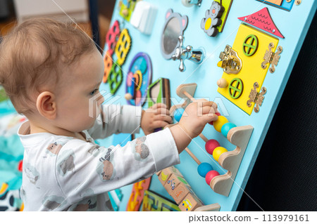 Profile of a cute baby playing with wooden elements on a busy board Profile of a cute baby playing with wooden elements on a busy board 113979161