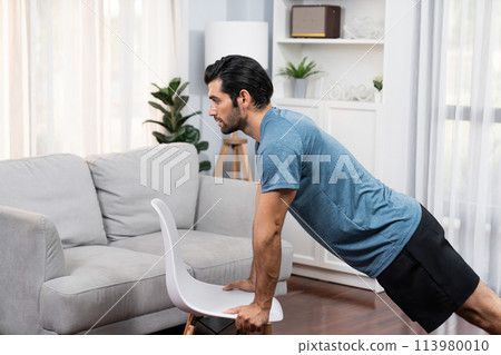 Athletic body and active sporty man using furniture for gaiety home exercise. 113980010