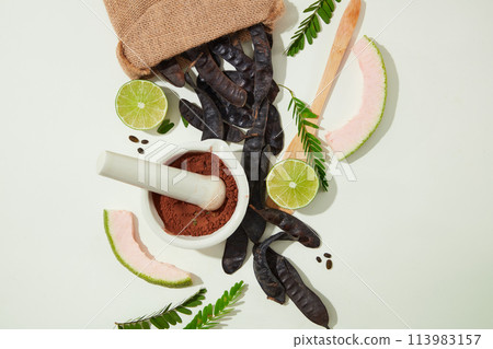 Above view photo with black locust pods, lemon, fern, wooden spoon, mortar and pestle with black locust powder inside. Copy space for text 113983157