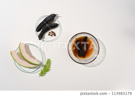 The dried black locust seed pods are soaked in a transparent bowl of water, a dish of grapefruit and a dish of black locust seed pods. Top view, white background with blank space The dried black locust seed pods are soaked in a transparent bowl of water, a dish of grapefruit and a dish of black locust seed pods. Top view, white background with blank space 113983179