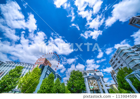 Yokohama cityscape in April, Japan. View of the ferris wheel and Tsuzuki Hankyu Railway in front of Center Kita Station, shining against the fresh greenery and blue sky. 113984509