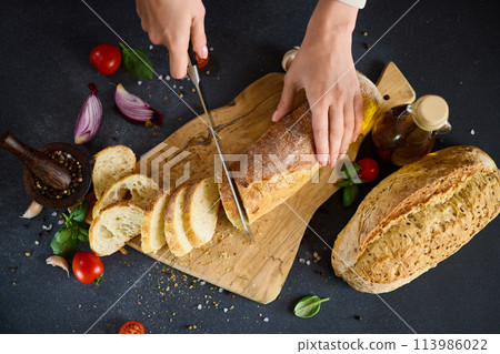 chef cutting Fresh bread on wooden cutting board on kitchen table chef cutting Fresh bread on wooden cutting board on kitchen table 113986022