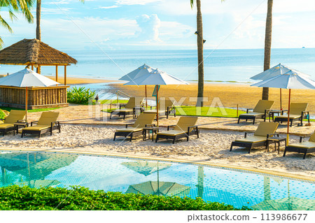 Beautiful luxury umbrella and chair around outdoor swimming pool in hotel and resort with coconut palm tree on sunset  or sunrise sky 113986677