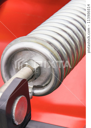 Steel silver spring as part of red agricultural machine. Technology 113986814