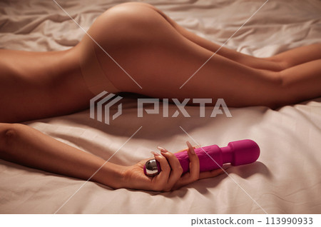 pink sex vibrator in hand of a woman girl with a sexy body and ass in underwear lying on white sheet on bed in bedroom. Sex toys for female satisfaction and orgasm pink sex vibrator in hand of a woman girl with a sexy body and ass in underwear lying on white sheet on bed in bedroom. Sex toys for female satisfaction and orgasm 113990933