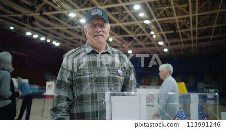 Elderly voter puts bulletin into box and starts look at camera 113991246