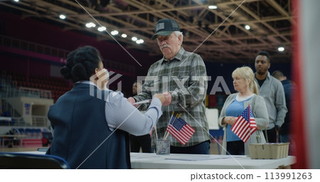 Elderly man talks with polling officer and takes vote bulletin 113991263