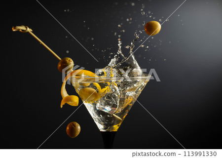 Classic dry martini cocktail with green olives and lemon peel on a black background. Classic dry martini cocktail with green olives and lemon peel on a black background. 113991330