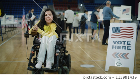 Woman with SMA smiles and looks at camera in polling station 113991439