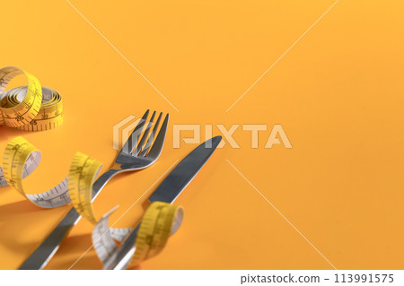 Fork and knife wrapped with measuring tape on yellow background. Weight loss and healthy concept 113991575