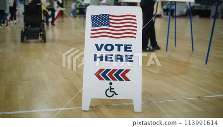 Vote here sign on floor. Woman in electric wheelchair comes to vote Vote here sign on floor. Woman in electric wheelchair comes to vote 113991614