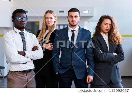 Confident diverse business team stands in modern office. African, Caucasian, Arabic, and Asian colleagues pose, strong corporate unity. Mixed race, gender equality at pro workplace. 113992967