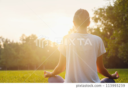 Young asian woman doing meditation in morning or evening at park, healthy woman relaxing and practicing yoga at city park. Mindfulness, destress, Healthy habits and balance concept 113993239