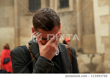 Young man outside, expressing fatigue and stress with a facepalm gesture. Concept of burnout 113993788