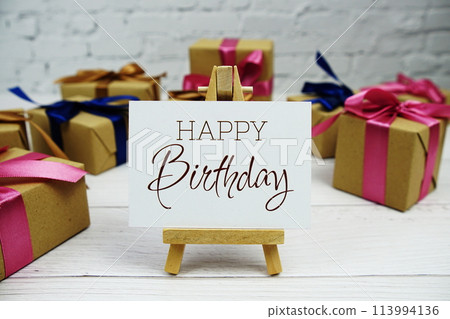 Happy Birthday text on paper card with gift box present on wooden background Happy Birthday text on paper card with gift box present on wooden background 113994136