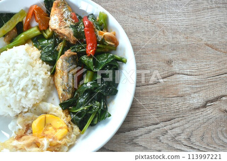 spicy stir fried Chinese kale with fish can in tomato sauce topping egg on plain rice in plate 113997221