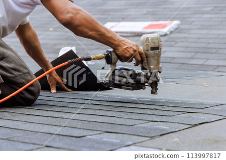 Air pneumatic nail gun used by roofer to install new asphalt bitumen shingles Air pneumatic nail gun used by roofer to install new asphalt bitumen shingles 113997817