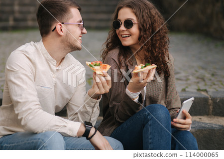 Young bloggers make selfie with slice of pizza in hands. Beautiful couple in sunglasses smile and kiss. Vegan fast food 114000065