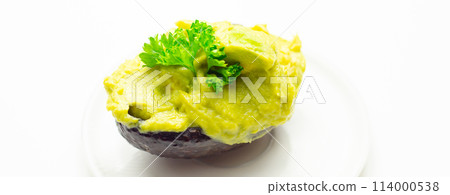 A green avocado with parsley on top sits on a white plate A green avocado with parsley on top sits on a white plate 114000538