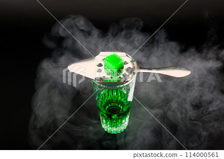 Green flavoured vodka called Absinthe served in a shot glass with a special spoon with white sugar cubes 114000561