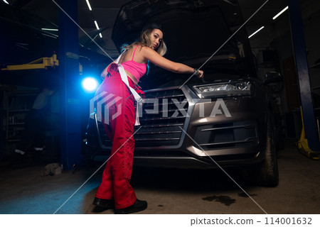a beautiful girl in a uniform repairs a car at a car service station 114001632