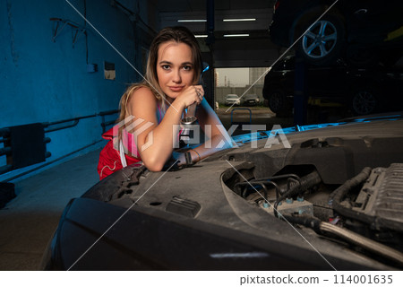a beautiful girl in a uniform repairs a car at a car service station a beautiful girl in a uniform repairs a car at a car service station 114001635