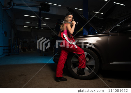 a beautiful girl in a uniform repairs a car at a car service station a beautiful girl in a uniform repairs a car at a car service station 114001652