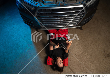 a beautiful girl in a uniform repairs a car at a car service station a beautiful girl in a uniform repairs a car at a car service station 114001656