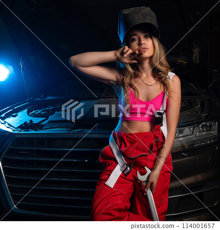a beautiful girl in a uniform repairs a car at a car service station a beautiful girl in a uniform repairs a car at a car service station 114001657