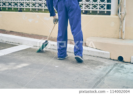 A male janitor sweeps a parking space next to a shopping center with a broom. City cleaning, janitor. High quality photo A male janitor sweeps a parking space next to a shopping center with a broom. City cleaning, janitor. High quality photo 114002004