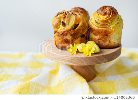 Freshly baked pastries are displayed on a wooden stand decorated with yellow flowers against a tartan background. Easter concept. 114002366