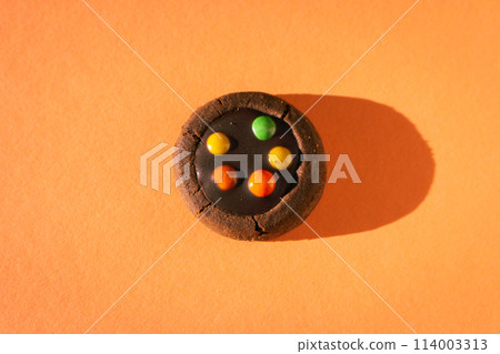 Brown cookie with colourful drops on peach fuzz baclground. Chocolate biscuit in sunlight on orange baclground. Dessert isolated with copy space. Minimal concept. Crunchy bakery.  114003313
