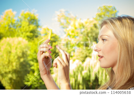 Woman sitting in park, using phone taking pictures Woman sitting in park, using phone taking pictures 114005638