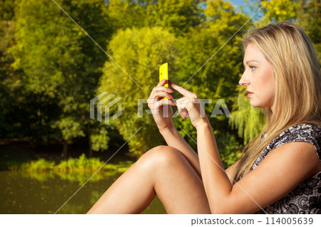 Woman sitting in park, using phone taking pictures Woman sitting in park, using phone taking pictures 114005639