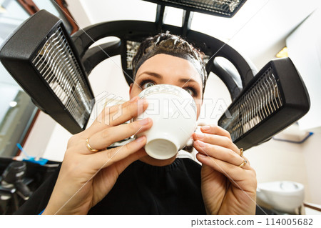 Woman in hairdresser drinking coffee under machine Woman in hairdresser drinking coffee under machine 114005682