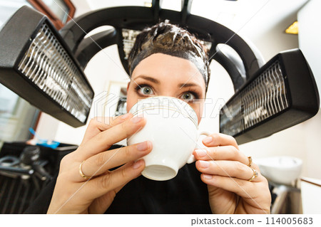 Woman in hairdresser drinking coffee under machine 114005683