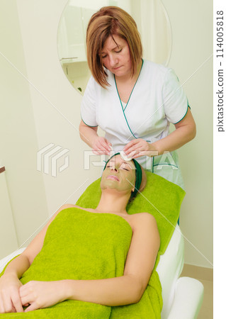 Beautician wiping off green mask on woman Beautician wiping off green mask on woman 114005818