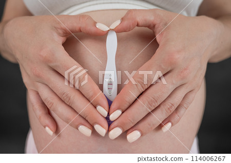 Caucasian woman holding a positive express pregnancy test against the background of her tummy. Caucasian woman holding a positive express pregnancy test against the background of her tummy. 114006267