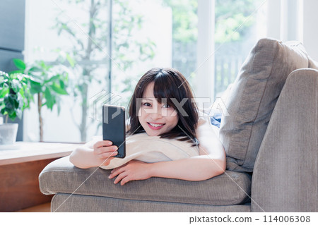 A young woman relaxing on a sofa and using a smartphone A young woman relaxing on a sofa and using a smartphone 114006308