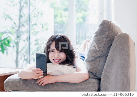 A young woman relaxing on a sofa and using a smartphone A young woman relaxing on a sofa and using a smartphone 114006310