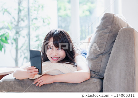A young woman relaxing on a sofa and using a smartphone A young woman relaxing on a sofa and using a smartphone 114006311