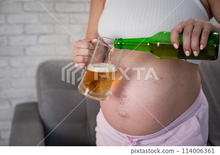 Faceless pregnant woman pouring beer into a glass. Faceless pregnant woman pouring beer into a glass. 114006361