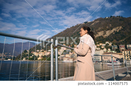 Young pretty woman on waterfront, admiring the lake of Como in Italy. Beautiful Alpine mountains on the background. People. Travel destinations. Tourism. People. Lifestyle Young pretty woman on waterfront, admiring the lake of Como in Italy. Beautiful Alpine mountains on the background. People. Travel destinations. Tourism. People. Lifestyle 114007575