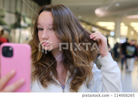 Portrait of a happy cheerful smiling young female student schoolgirl with long hair standing looking at the camera taking a selfie. High quality photo 114008265