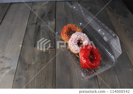 Three red donuts in a plastic box on a gray background with space for copyspace text. Donut Day Candy Delivery American Food 114008542