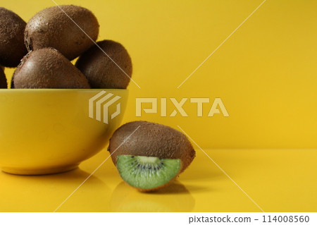 Still life of fruit trending illuminatiited yellow kiwi in a bowl plate of yellow and next pieces of kiwi yellow background with a place to text copyspace Still life of fruit trending illuminatiited yellow kiwi in a bowl plate of yellow and next pieces of kiwi yellow background with a place to text copyspace 114008560